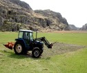 A tractor with forklift attachment on front driving along a croft.