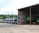 Farm steading with a combine parked in a shed and wrapped bales stacked next to it.