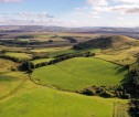 Aerial photograph of grass fields and hills, with hedges and woodland along boundaries and on the side of hill areas.