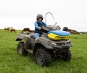 A female farmer on a quadbike, wearing safety gear, in a field of cattle.