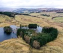 Farm land near Blair Atholl, including an area of wetland with trees surrounding it. There are hills across the backdrop of the landscape.