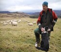 A shepherd and his sheepdog looking out over a flock of sheep