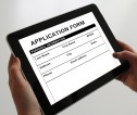 Image of hands holding up electronic tablet with 'Application Form' in bold text on the screen